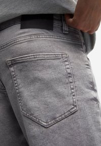 Lichtgrijze denim jeans met een gladde textuur, voorzien van een enkele achterzak en een donkerleren merklabel op de tailleband.