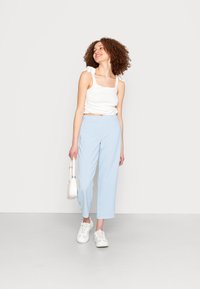 Top cropped branco com alças atadas, calças de cintura alta azul claro e ténis brancos. Design simples com um corte relaxado.