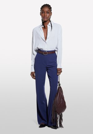 Blouse bleu clair avec un décolleté en V profond, pantalon navy à jambes larges, ceinture marron et sac à main à franges marron. Textures lisses et couleurs contrastées.