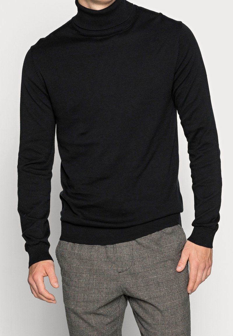 Schwarzer Rollkragenpullover aus feinem Strickmaterial, mit langen Ärmeln und geripptem Saum. Kombiniert mit karierter Hose.