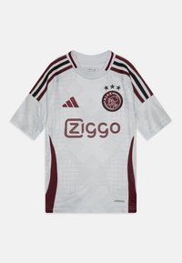 Valkoinen jalkapallopaita, jossa on maroon-väriset yksityiskohdat, geometristen kuvioiden kanssa, kolmonen mustaa raitaa olkapäillä ja logo. Valmistettu hengittävästä kankaasta.