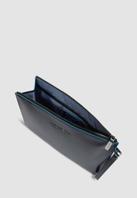 Bolso de mano de cuero negro con cierre de cremallera, ribete azul a lo largo del borde y un interior forrado que muestra una etiqueta.