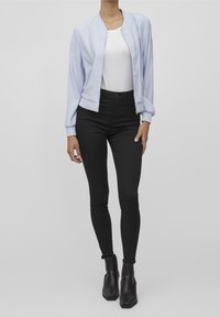Světle modrá bomber bunda s předním zipem, bílý tričko, černé úzké džíny a černé kotníkové boty. Hladké textury, přiléhavý střih.