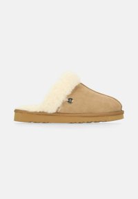 Suedeslay slipper i tan med en fluffig krämfärgad fårskinns foder. Har en texturerad gummisula och en rund metallisk logotypaccent.