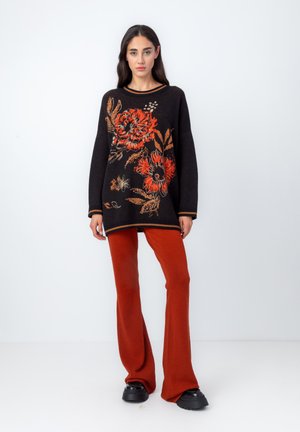 Black sweater with orange floral embroidery, long sleeves, and ribbed cuffs, paired with rust flared pants and chunky black shoes.