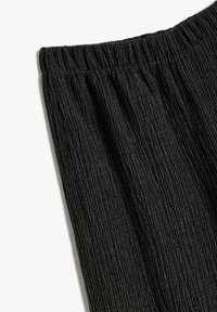 Zwarte, gestructureerde stof met een verticaal plooipatroon. Elastische tailleband aan de bovenkant. Het materiaal lijkt lichtgewicht en valt soepel.