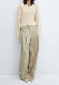 Beige knit sweater with a lace-up neckline, paired with high-waisted, wide-leg khaki trousers featuring white trim at the cuffs.