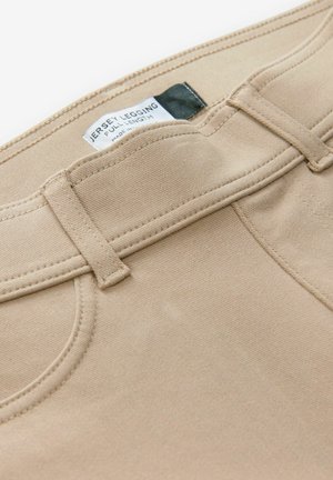 Bézs színű jersey leggings sima textúrával, lapos derékkal és varrott elülső zsebekkel. A címke felirata: "Jersey Legging Full Length."
