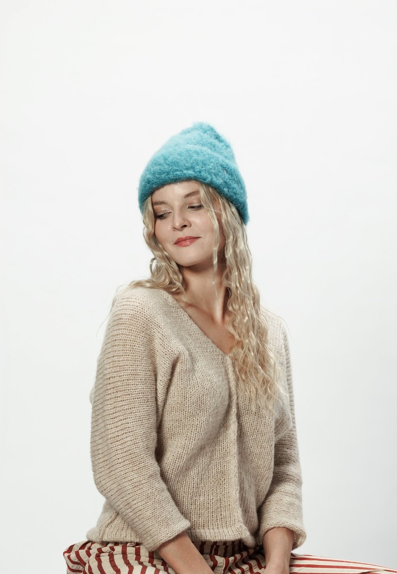 Jasnoniebieska filcowa czapka, miękka w dotyku. Beżowy sweter dziany z dekoltem w serek i rękawami o długości trzech czwarte. Spodnie w paski wprowadzają wzór.