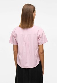 Kortärmad, rosa bomullsskjorta med rundad nederkant och en plissér på baksidan. Har en enkel design och lätt textur, lämplig för avslappnad användning.