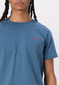 Kék pamut póló kerek nyakkivágással és rövid ujjakkal. Az elülső bal oldalon található egy kis vörös Levi's logo folt.