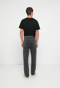 Camiseta negra combinada con pantalones de mezclilla gris. Los vaqueros tienen un corte relajado, dos bolsillos traseros y un sutil logo cerca de la cintura.