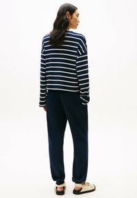 Maglia a maniche lunghe a righe navy e bianche abbinata a pantaloni jogger navy uniformi. Vestibilità casual con silhouette rilassata e tessuto leggero.