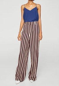 Débardeur bleu à col en V associé à un pantalon large avec des rayures longitudinales bordeaux et crème. Tissu lisse et coupe ajustée.