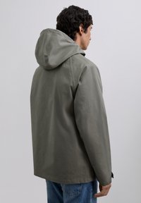 Chaqueta con capucha en un verde oliva apagado, que presenta un diseño sencillo, textura suave y un corte relajado, vista desde la parte trasera.