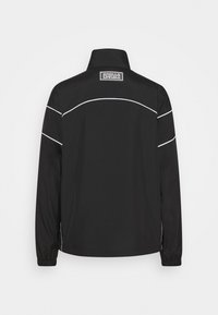 Chaqueta negra de manga larga, con un cuello alto, detalles de ribete blanco y una etiqueta en el escote. Textura suave, diseño minimalista.