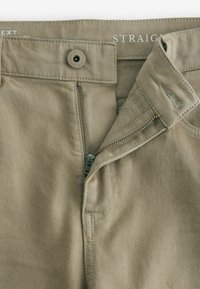 Beige lige bukser med lynlåslukning, knaplukning og subtil tekstur. Har tonalt syning og et mærke syet indeni taljebåndet.