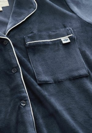 Navy blue, soft fabric pajama shirt with white piping along the collar and pocket. Features buttons and a left chest pocket.