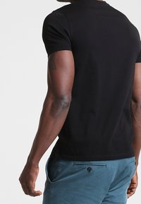 Schwarzes T-Shirt mit kurzen Ärmeln, Rundhalsausschnitt und taillierter Silhouette, kombiniert mit türkisfarbenen Shorts, die einen Knopfakzent und Seitentaschen haben.