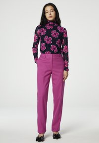 Langermige, aansluitende coltrui in marineblauw met grote roze bloemenprint, gecombineerd met hooggetailleerde, op maat gemaakte roze broek en schoenen met zwarte strikaccenten.