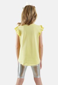 Gul kortærmet top med rynkede detaljer, parret med skinnende sølvleggings, der viser en glat tekstur og enkelt design.