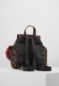Sac à dos en cuir noir avec des accents marron à motifs, une poignée supérieure, des bretelles réglables et un détail pompon en fausse fourrure rouge sur le côté.