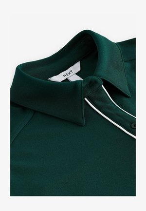 Dark green polo shirt with a flat collar, contrasting white trim along the placket, and a button closure. Soft, smooth fabric texture.