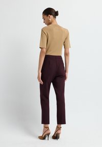 Haut marron à manches courtes associé à un pantalon bordeaux ajusté, avec une texture lisse. Porté avec des sandales à talons hauts marron.