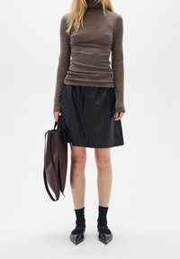 Brun polotröja, svart läderkjol, svarta ankelsocker, svarta spetsiga skor, håller en stor brun tote-väska. Enkel design, subtila texturer.