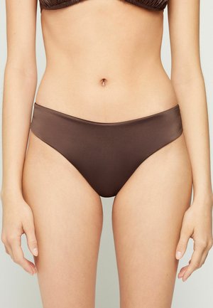 Mujer con braguita de bikini marrón y top de bikini con volantes, mostrada desde la cintura hasta la parte superior de los muslos sobre un fondo liso.