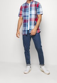 Camicia a maniche corte a quadri con colori rosso, blu e bianco e colletto con bottoni. Abbinate a jeans blu scuro e sneakers bianche.