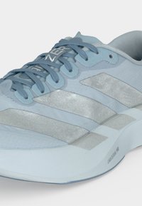 Chaussure de sport bleu clair avec des bandes Adidas grises, des lacets bleus, et le texte « LIGHTSTRIKE PRO » sur le côté de la semelle.