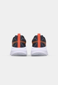 Black and orange athletic shoes feature a textured upper, white sole, and a prominent orange pull tab at the back.