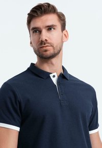 Námořnická modrá polokošile s bílým límečkem a manžetami, s trojím knoflíkovým zapínáním. Vyrobena z texturované bavlněné tkaniny. Úzký střih.