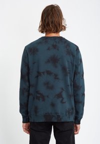 Sweat-shirt bleu canard foncé avec un motif de tie-dye noir. Matière en coton, col rond classique, manches longues, poignets et ourlet côtelés.
