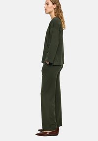 Zielono-oliwkowy zestaw loungewear z luźną bluzką z długim rękawem i szerokimi spodniami z bocznymi kieszeniami, zestawiony z brązowymi czółenkami w szpic.