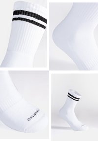 Calcetines deportivos de algodón blancos con rayas negras en la parte superior, textura acanalada y un logo impreso en la zona de los dedos. Longitud a mitad de pantorrilla.