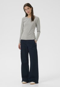 Maglietta grigia a maniche lunghe con scollatura rotonda, abbinata a pantaloni a gamba larga blu scuro, dotati di tasche laterali e orli risvoltati. Insieme casual.