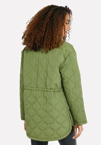 Giacca verde trapuntata caratterizzata da una vestibilità lunga e rilassata, con cuciture a motivi curvi, fessure laterali e vita smilza per definire la forma.
