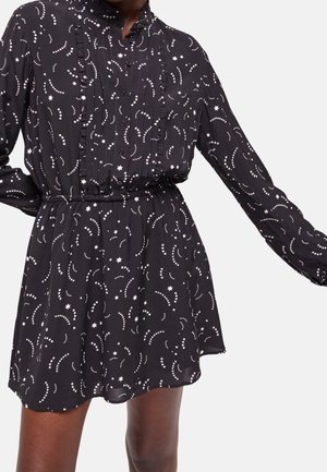 Schwarzes langärmeliges Kleid mit weißen Stern- und gepunkteten Wirbelmustern, durchgeknöpft, elastischer Taille und Rüschenverzierung an der Brust.
