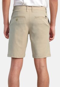 Beige shorts featuring a cotton blend, straight cut, two back pockets with button closure, and a folded hem. Designed for casual wear.