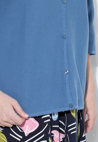 Modrý texturovaný cardigan s knoflíkovým zapínáním, který má tříčtvrteční rukávy. Spárován s sukní s květinovým vzorem v tmavých barvách.