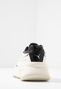 Sneaker Puma con una combinazione di colori bianco e nero, caratterizzate da una tomaia in pelle texturizzata, design snello e logo visibile sul tallone.