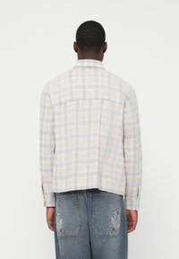 Wzorzysta koszula w beżowo-niebieskie kratki. Posiada standardowy kołnierzyk, mankiety na guziki oraz luźny krój. Tkany materiał o gładkiej teksturze.