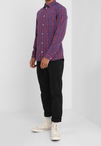 Camicia a maniche lunghe da uomo in fantasia a quadri rossi e blu, in cotone, con design slim fit e polsini con bottone, abbinata a pantaloni neri.