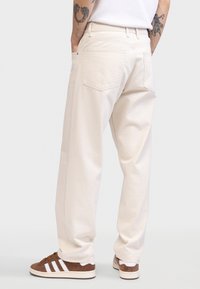 Ljusbeige jeans med vida ben i denim, med bakfickor och hög midja, kombinerade med bruna och vita sneakers.