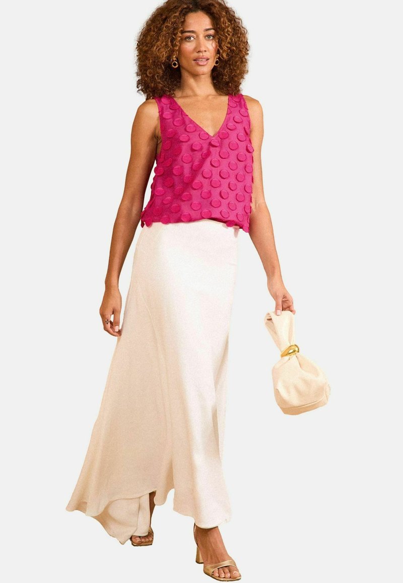 Top roz fără mâneci, cu aplicații rotunde texturate, asortat cu o fustă albă fluidă. Accesoriile includ o poșetă crem și sandale aurii.