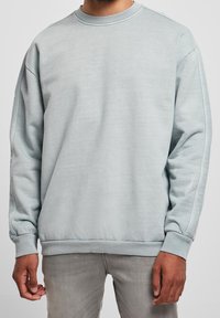 Světle modrá mikina s kulatým výstřihem, žebrovanými manžetami a lemem. Má uvolněný střih a měkkou, texturovanou látku.