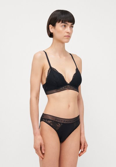 Melna mežģīņu bralette ar trīsstūrveida formu, regulējamiem siksniņām un joslu ar uzrakstu "POLO RALPH LAUREN." Atbilstošas melnas mežģīņu apakšbikses.