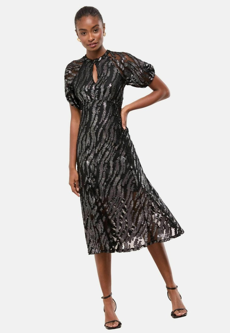 Rochie midi neagră din material transparent texturat, cu mâneci bufante și decolteu cu orificiu. Prezintă o siluetă fluidă și accente metalice subtile.